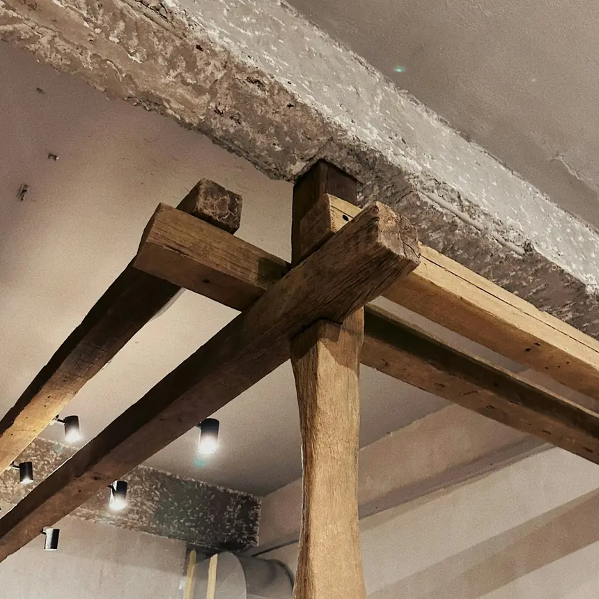 Stare dębowe belki i słup pod jasnym stropem poddasza